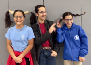 An adult and two Mayflower students posing together indoors
